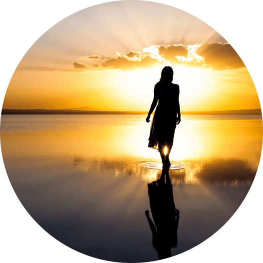 A woman walking on the beach at sunset.